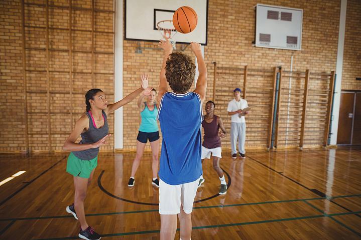 Foto de niños de secundaria jugando baloncesto en un gimnasio.