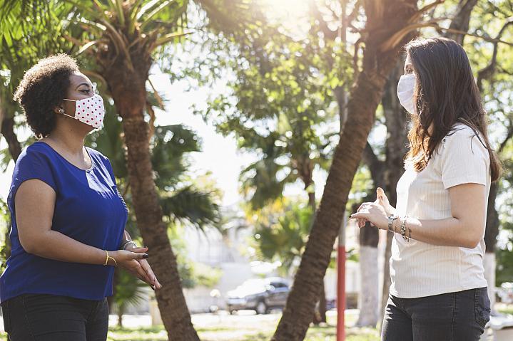 Una foto de dos mujeres con mascarillas mientras hablan al aire libre y practican el distanciamiento social.