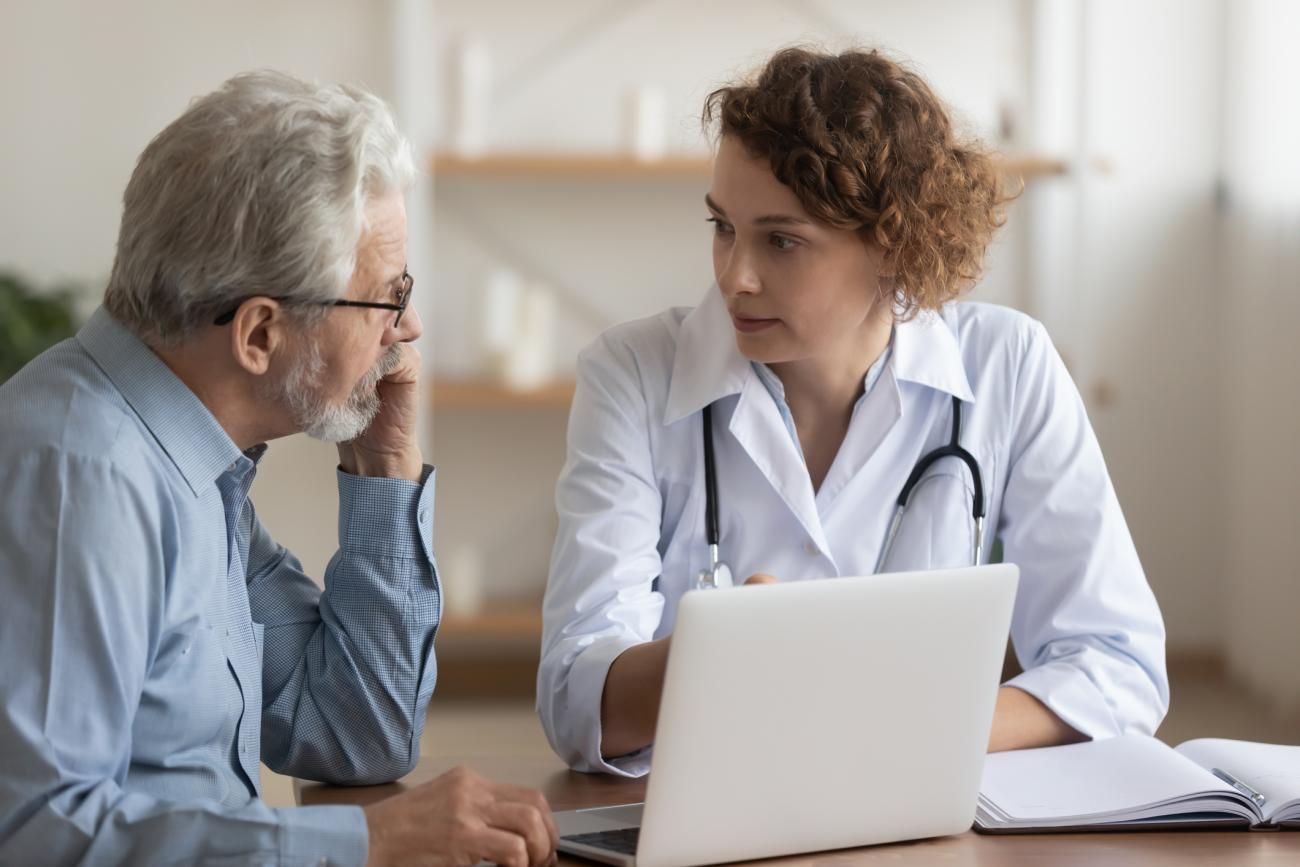 Foto de una médica hablando con un paciente masculino mayor.