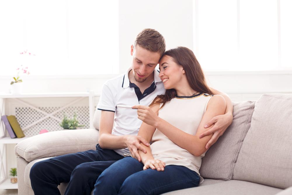 Foto de una pareja joven mirando una prueba de embarazo en el sofá