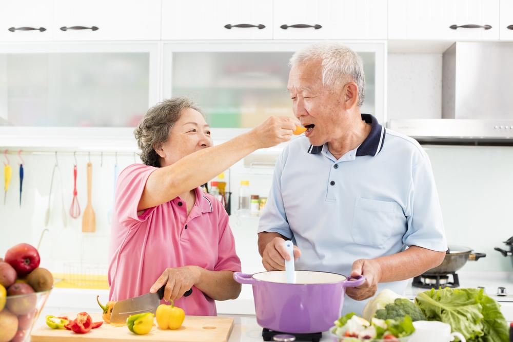 Foto de una pareja de adultos mayores cocinando verduras.