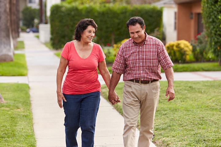 Pareja hispana de edad avanzada caminando de la mano por una acera.