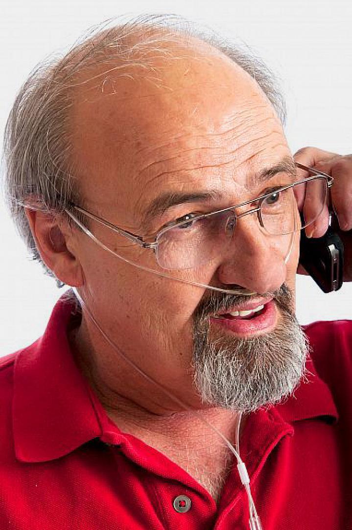 Hombre hablando por teléfono mientras respira oxígeno a través de una delgada sonda nasal.