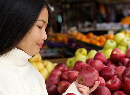 Una mujer en una tienda de comestibles mirando manzanas.