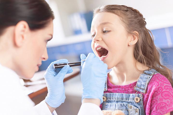 Doctora examinando la garganta de una niña con una espátula y una linterna