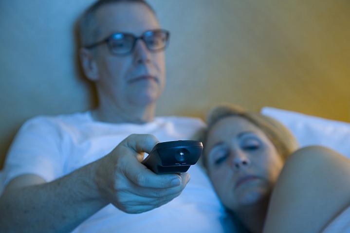 Una pareja soñolienta mira televisión en la cama