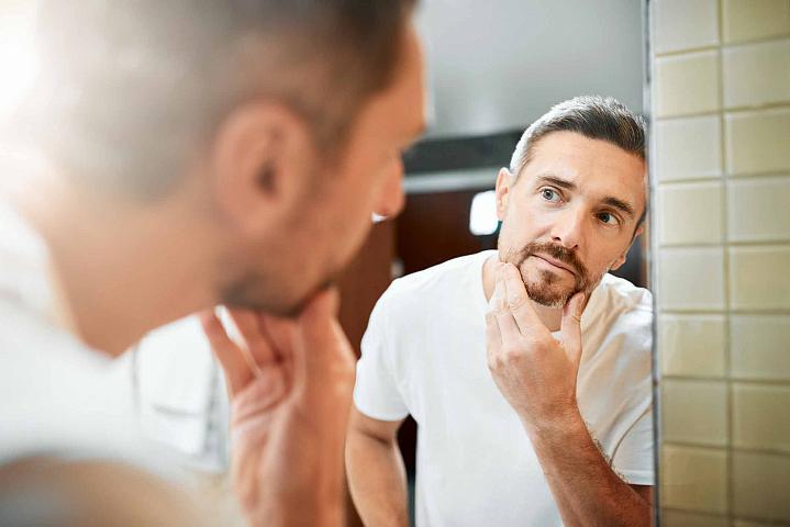 Foto de un hombre mirando las canas de su barba a través del espejo