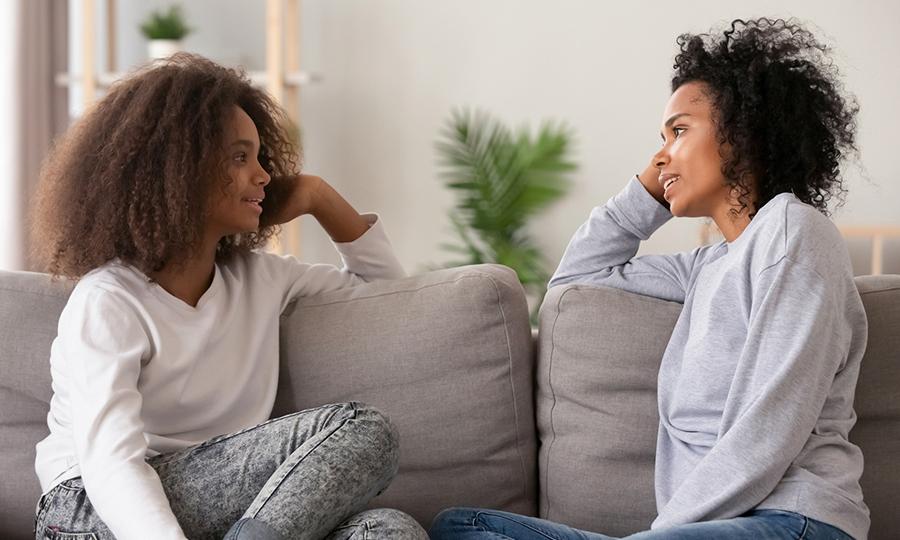 Foto de una madre escuchando a su hija adolescente mientras está sentada en el sofa