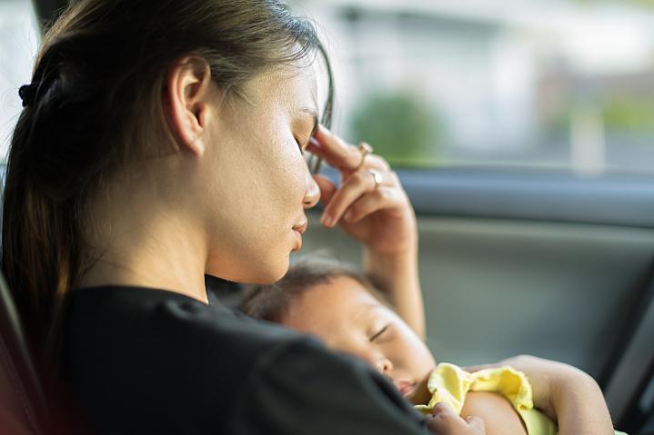 Foto de una mamá estresada que trata de tomar una siesta con su bebé en el automóvil