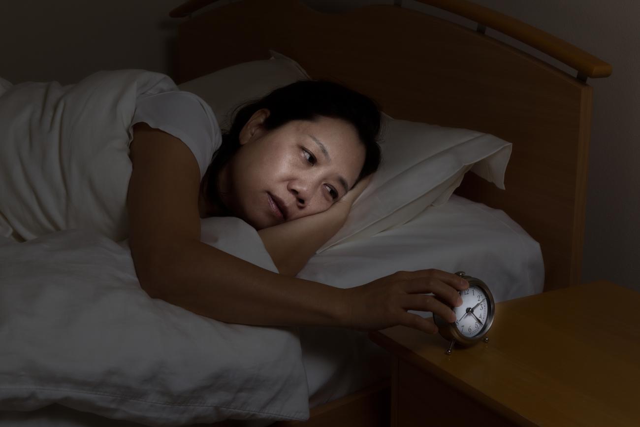 Imagen de una mujer despierta en la cama tocando el despertador