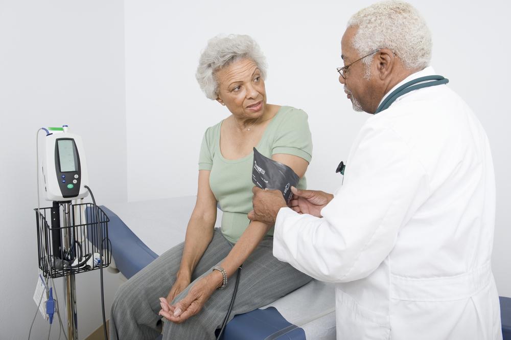 Imagen de un médico midiendo la presión arterial de una mujer negra de edad avanzada
