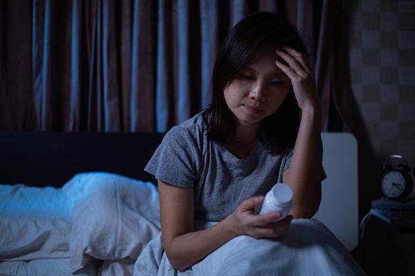 Foto de una mujer sentada en la cama leyendo un frasco de pastillas