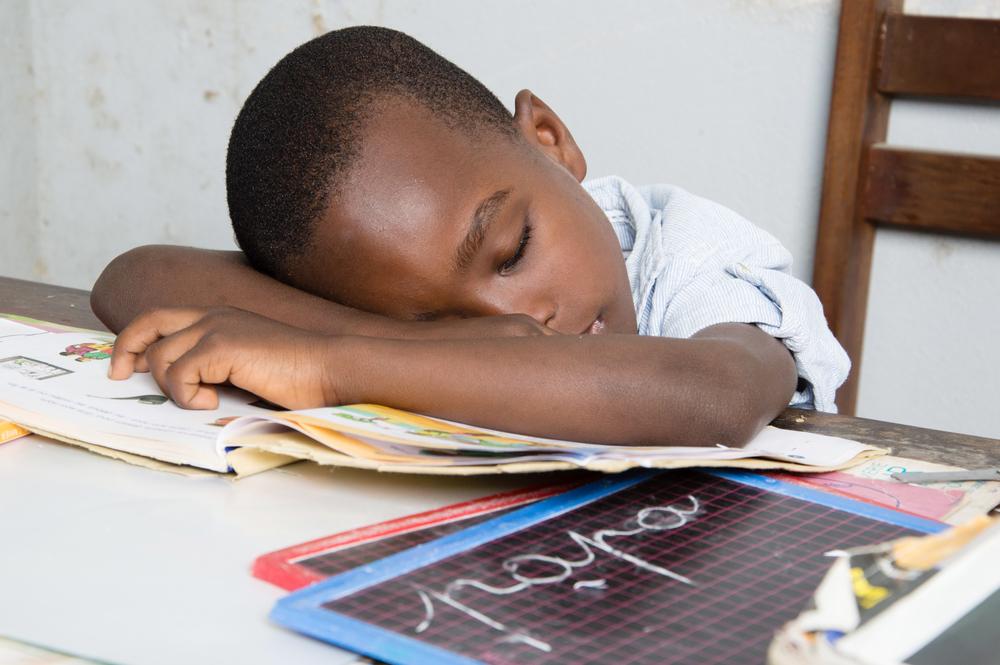Foto de un niño dormido en su escritorio con la cabeza sobre un libro.