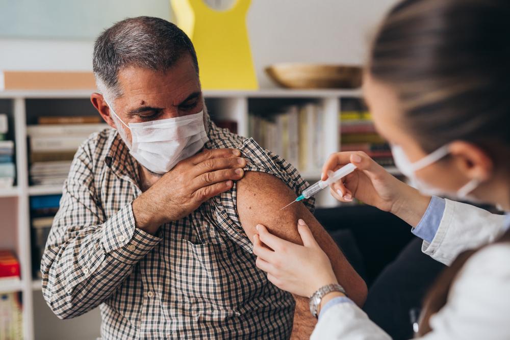 Foto de una persona con una máscara que recibe una vacuna COVID-19 de su proveedor de atención médica