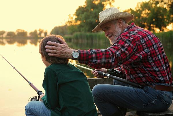 Imagen de un hombre conversando con su nieto mientras pesca.