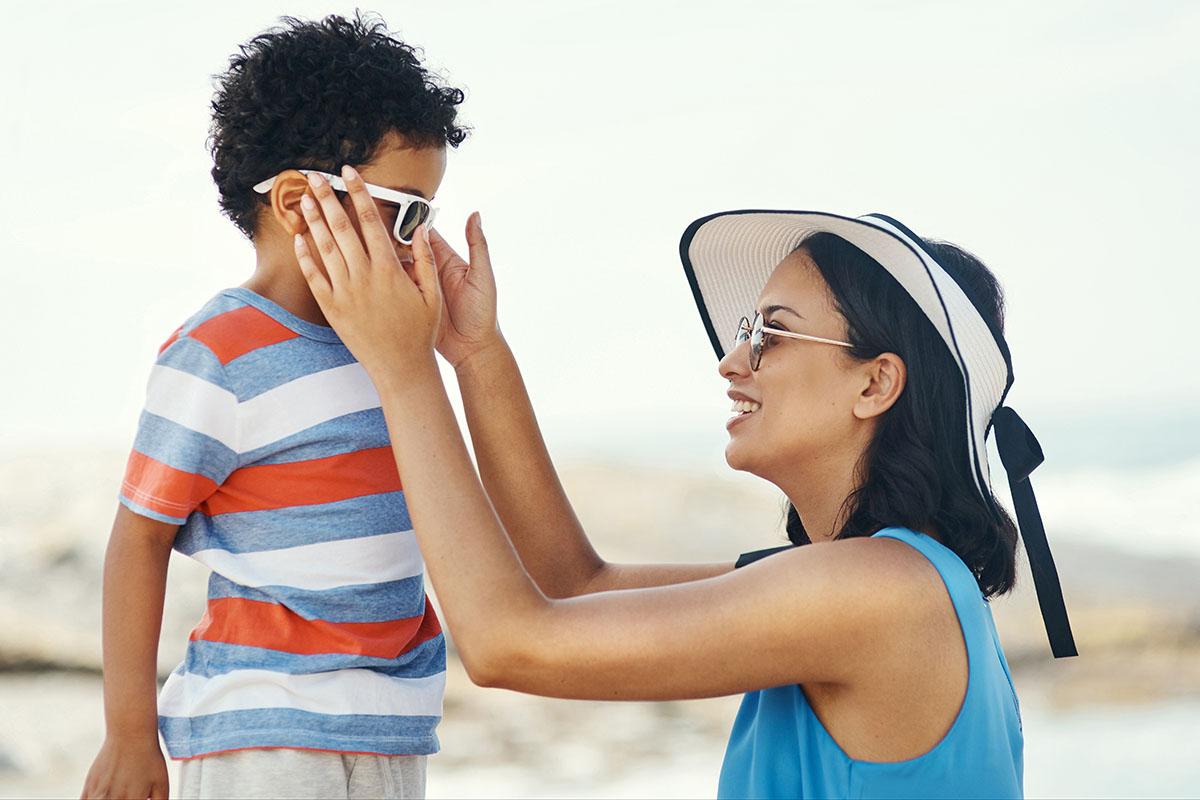 Imagen de una madre que le pone gafas de sol a su hijo.