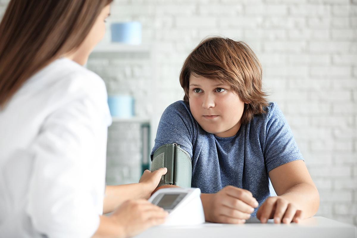 Imagen de un niño con sobrepeso al que un profesional de la salud le controla la presión arterial