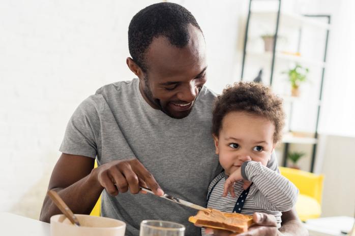 Imagen de un padre con su hijo pequeño untando una tostada con mantequilla de maní.