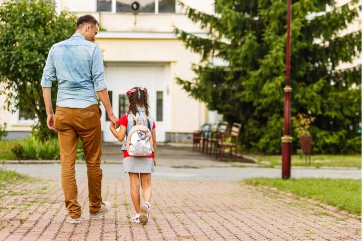 Imagen de un padre llevando a su hija de la mano a la escuela.