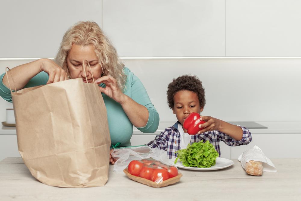 Una madre y su hijo están sacando alimentos saludables desde una bolsa de papel para compras.