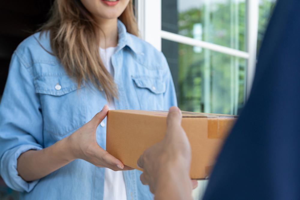 Fotografía de una mujer recibiendo un paquete de parte de un empleado de correos.