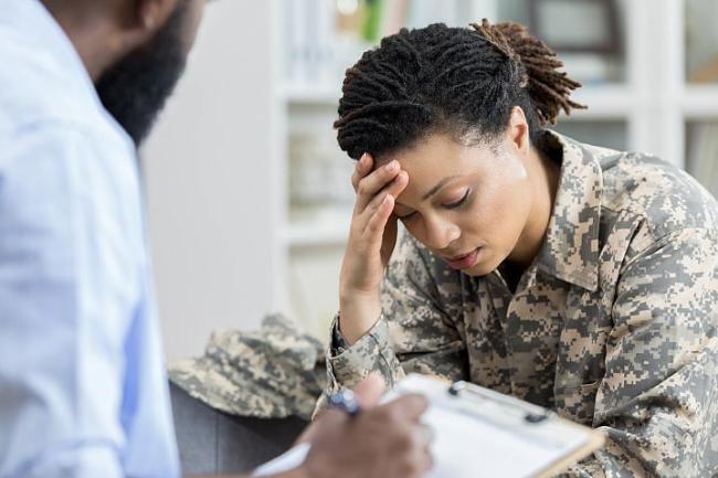 Foto de una veterana militar tomándose la cabeza en una cita con un profesional de la salud.