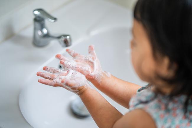Fotografía de una niña pequeña lavando sus manos con agua y jabón.