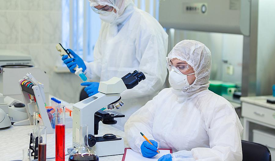 Dos científicos que usan equipo de protección personal trabajan en una estación de laboratorio con un microscopio y muestras.