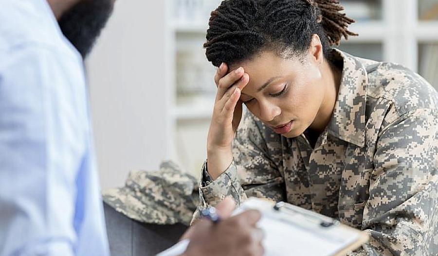 Foto de una veterana militar tomándose la cabeza en una cita con un profesional de la salud.