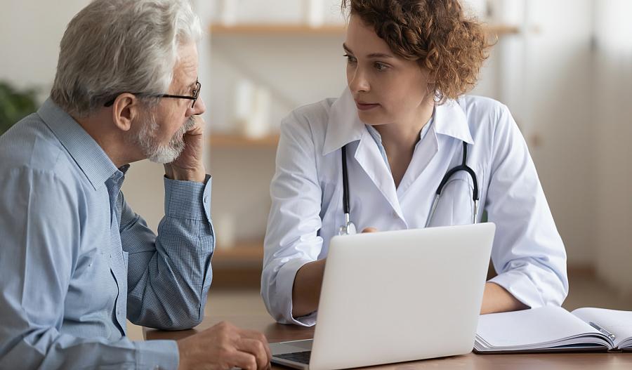 Foto de una médica hablando con un paciente masculino mayor.