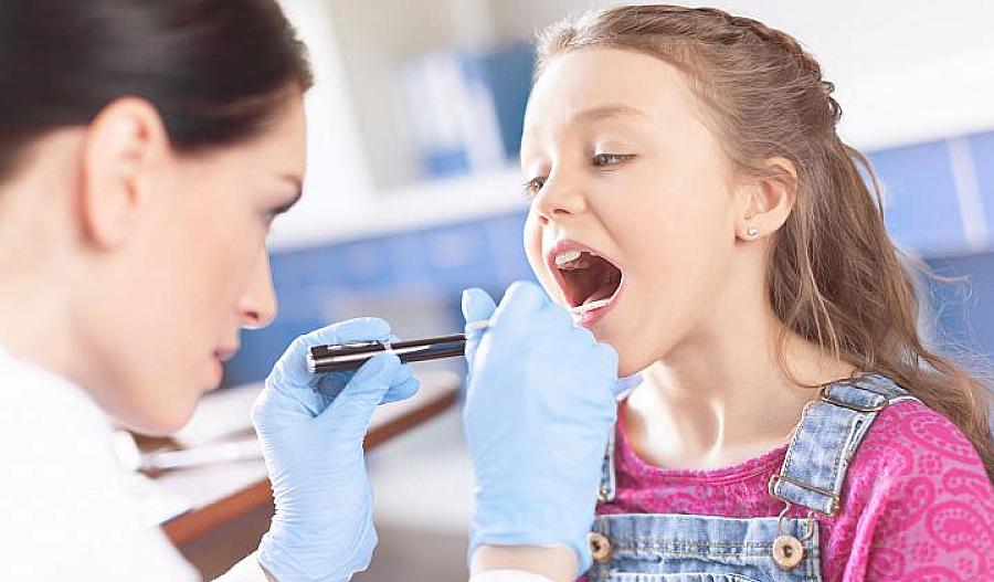 Doctora examinando la garganta de una niña con una espátula y una linterna