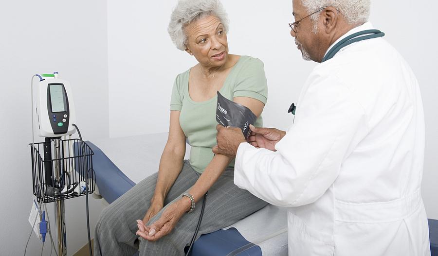 Imagen de un médico midiendo la presión arterial de una mujer negra de edad avanzada