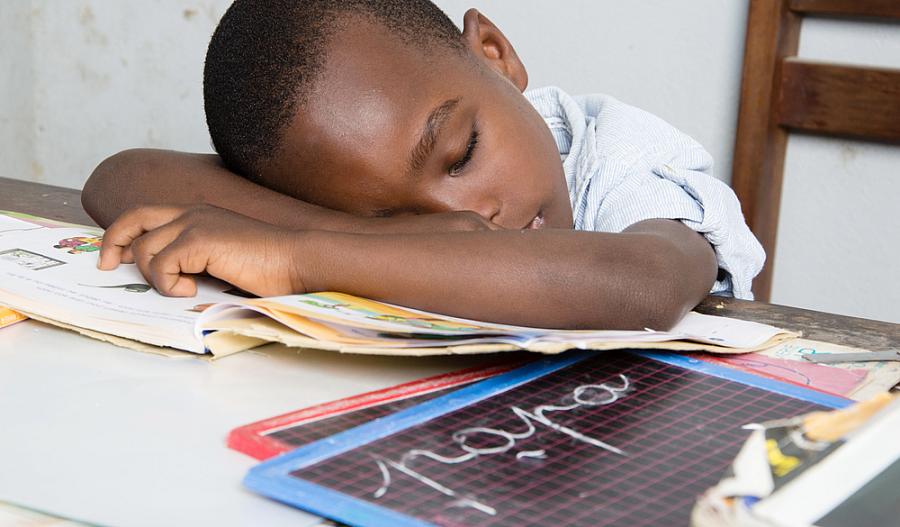 Foto de un niño dormido en su escritorio con la cabeza sobre un libro.