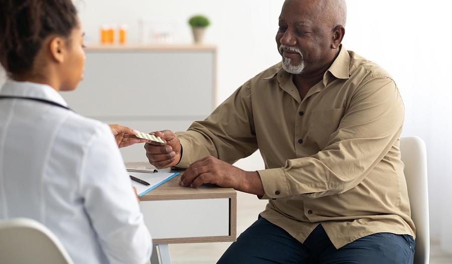 Foto de un proveedor de atención médica que le entrega un paquete de pastillas a un paciente adulto mayor.