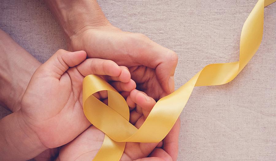 una foto de las manos de un adulto y un niño sosteniendo una cinta amarilla para representar la concientización sobre el cáncer infantil.