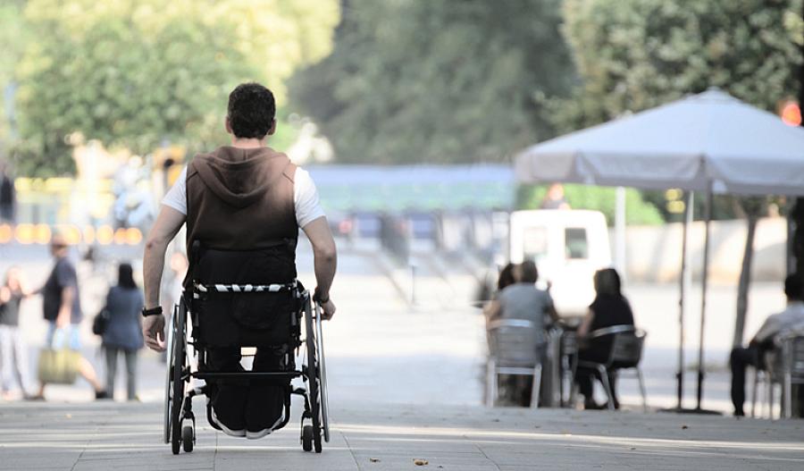 Imagen de un trabajador de salud que empuja a una persona con ELA en una silla de ruedas.