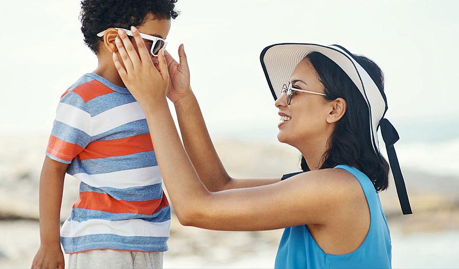 Imagen de una madre que le pone gafas de sol a su hijo.
