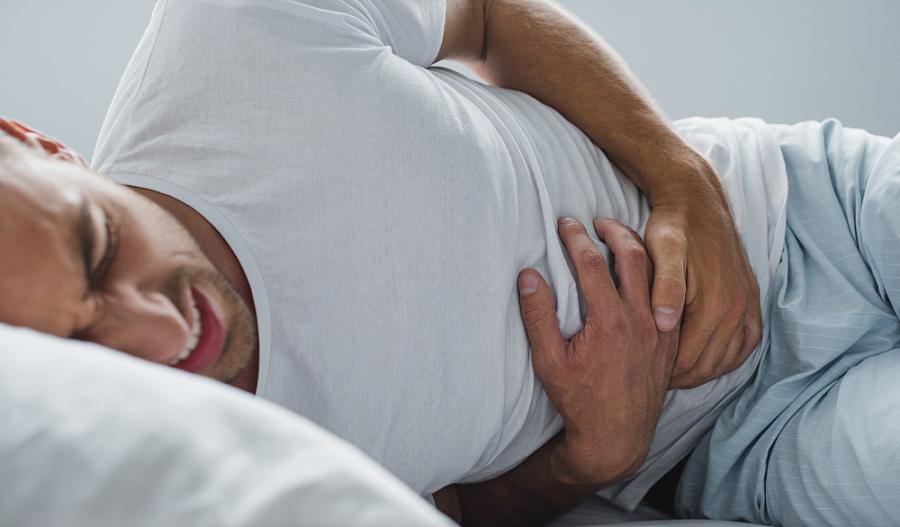 Foto de un hombre acostado de lado, sintiendo dolor y con su mano puesta en el estómago.