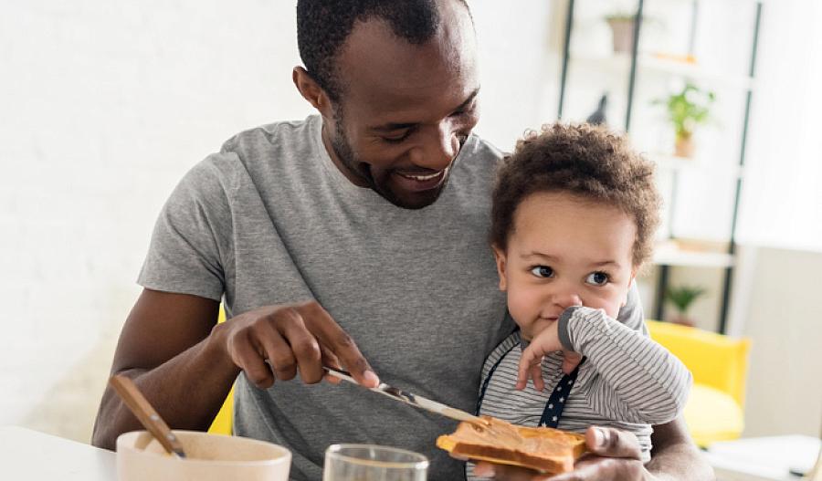 Imagen de un padre con su hijo pequeño untando una tostada con mantequilla de maní.