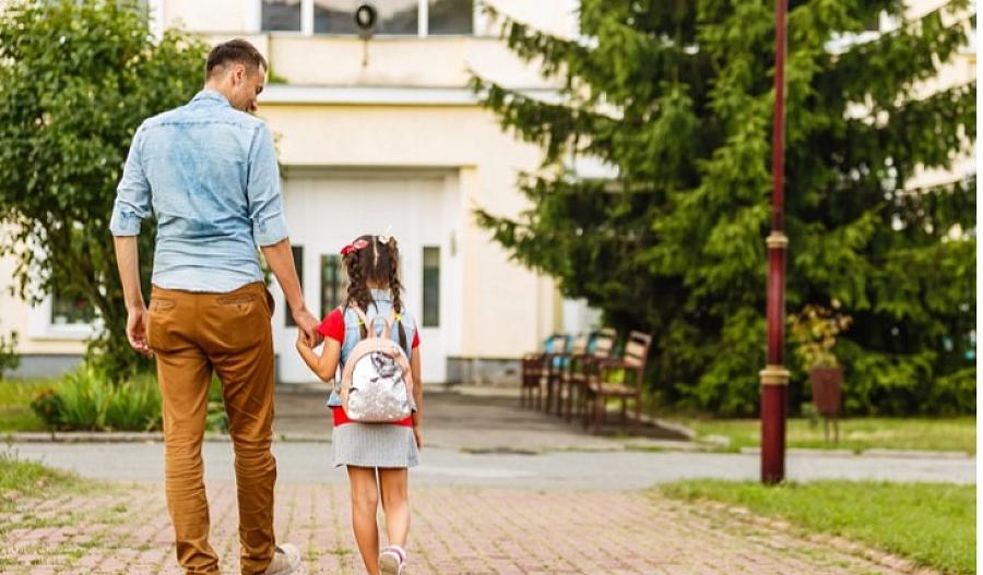 Imagen de un padre llevando a su hija de la mano a la escuela.