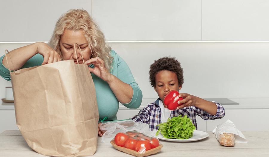 Una madre y su hijo están sacando alimentos saludables desde una bolsa de papel para compras.