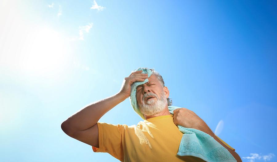 Una fotografía de un hombre adulto mayor bajo el sol, secando su frente con una toalla.