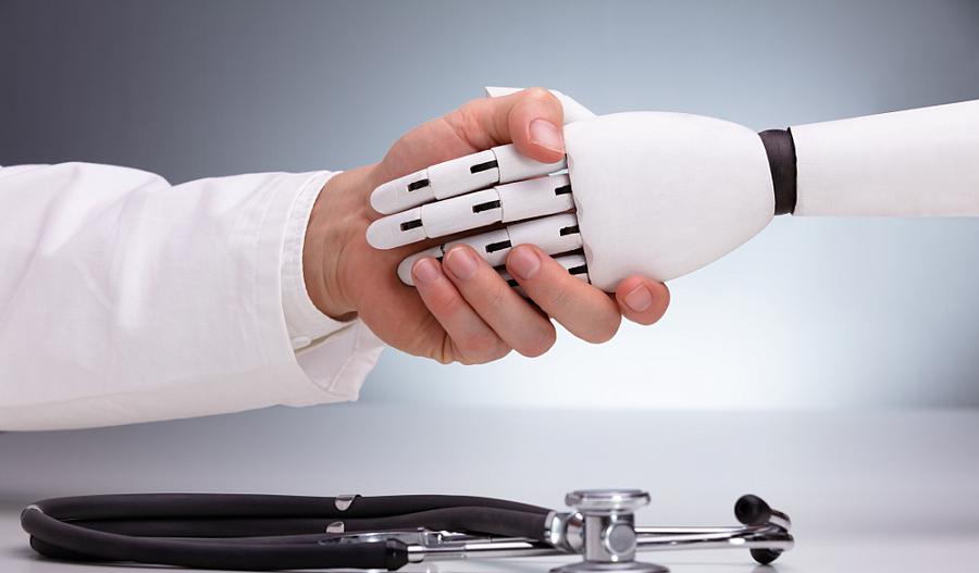 Foto de un apretón de manos entre un doctor y un robot. Un estetoscopio está ubicado por debajo de ambas manos sobre una mesa. 