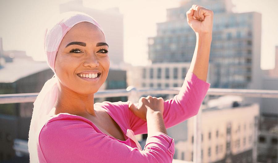 Una mujer con un pañuelo en la cabeza que parece una paciente de cáncer levanta el brazo en el aire en una pose que muestra sus músculos.