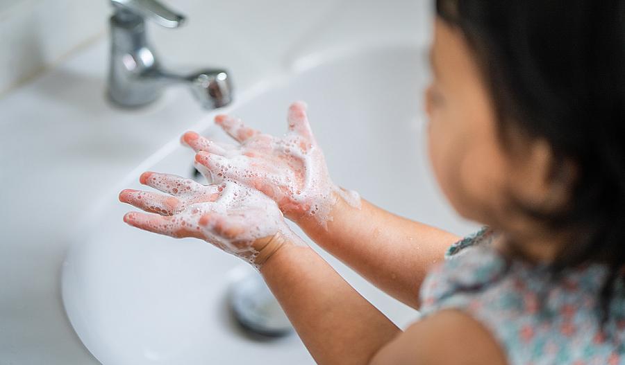 Fotografía de una niña pequeña lavando sus manos con agua y jabón.