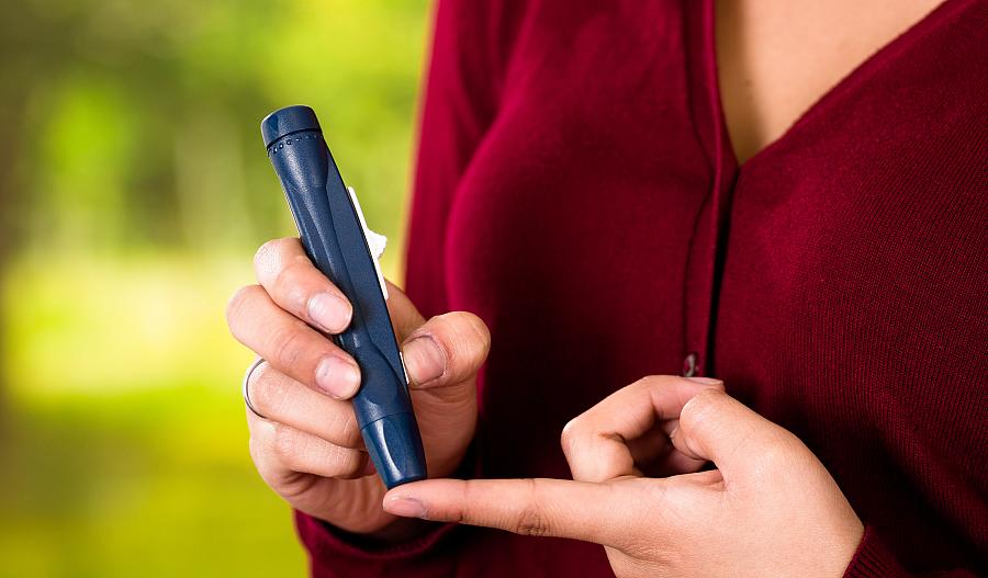 Una mujer en un suéter rojo se mide el nivel de azúcar en la sangre con un glucómetro.